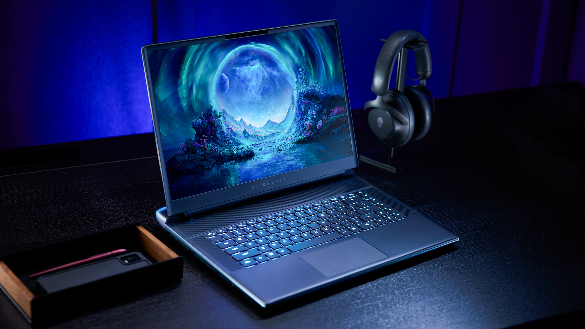 An Alienware Area-51 Laptop on a desk next to a headset and a phone. 